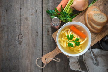 Chicken soup with noodles and carrot in white bowl.