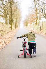 Little child boy on bicycle in park outdoor. A child is riding a children's bike with training support wheels 