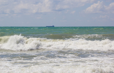 Big waves are rolling on the shore. The ship sails the stormy sea
