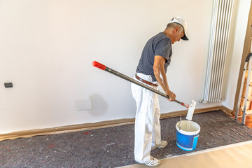Whitewasher man with paint roller and bucket in renovation new room for dyeing in white. © bennymarty