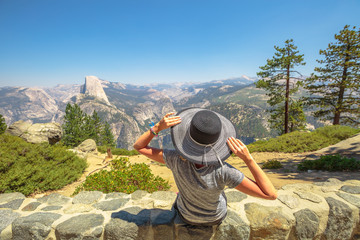 Traveler woman relaxing at Glacier Point in Yosemite National Park, California, United States. Glacier Point: Half Dome, Liberty Cap, Yosemite Valley and Nevada Fall. Summer travel holiday.