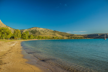 Mediterranean sea shore bay beautiful landscape with vivid water green and blue surface and rock horizon background in summer warm sultry weather