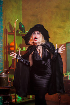 Image of screaming witch in black hat, dress on background of rack with pumpkin and crow