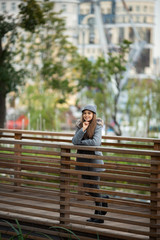 Photo of girl in gray hat and coat on wooden bridge in city