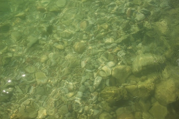 fuzzy underwater stones sea bottom background from above through small water surface waves, copy space