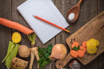 Ingredients for cooking: vegetables, spices and a notepad on the wooden background. Copy space.