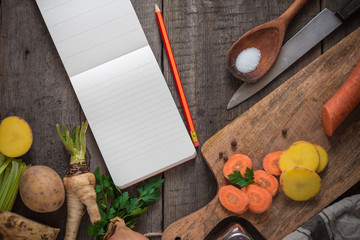 Ingredients for cooking: vegetables, spices and a notepad on the wooden background. Copy space.