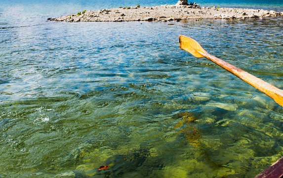 Oar of boat touching water and causing splash and ripples in the water A wooden paddle on a boat Blade of wooden kayak or canoe paddle Water splash   - Powered by Adobe