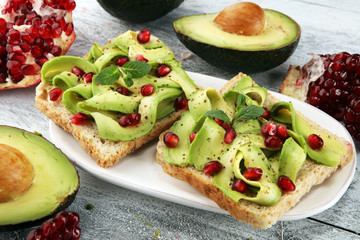 sliced avocado and ripe pomegranates on toast bread with spices and avocado.