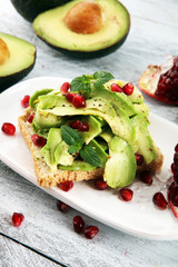 sliced avocado and ripe pomegranates on toast bread with spices and avocado.