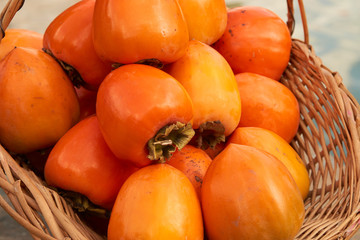 Persimmon fruits and persimmon leaves in a wicker basket. Agriculture and harvesting concept