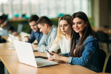 Group of college students studying in the school library, a girl and a boy are using a laptop and connecting to internet. Girl to the camera