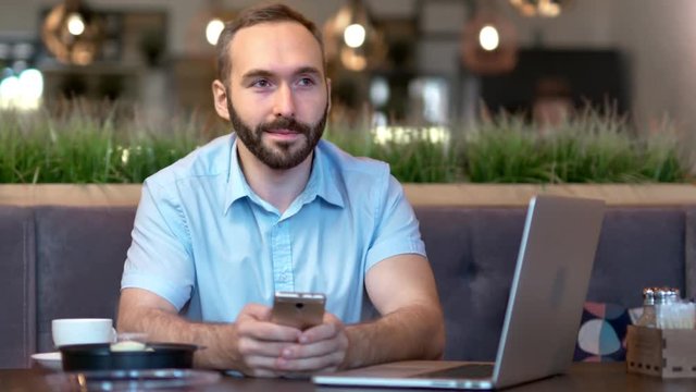 Portrait of smiling young businessman enjoying break chatting typing message using smartphone