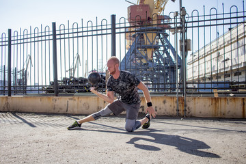 Young bearded male athlete training in industrial zone in sunny day, kettlebells exercises outdoors, urban background