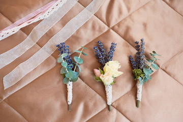 Wedding decor. Beautiful rose bouquet for a bride and three boutonnieres lie on the bed
