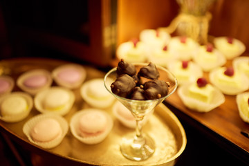 Wedding candy bar service. Delicious macaroons, cookies, pieces of cake and other sweets with chocolate, berries and cream served on the dinner table