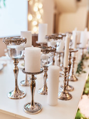 Wedding table serivce. Candles on silver vases and glasses with water stand among white flowers on wedding dinner table