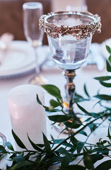 Wedding table serivce. Candles on silver vases and glasses with water stand among white flowers on wedding dinner table
