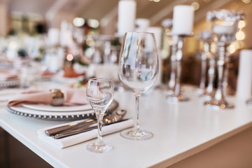 Wedding table serivce. Candles on silver vases and glasses with water stand among white flowers on wedding dinner table
