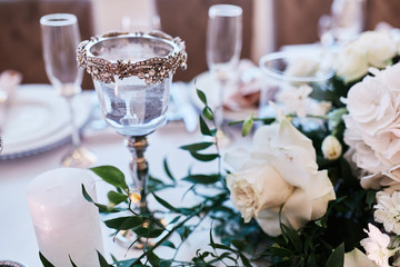 Wedding table serivce. Candles on silver vases and glasses with water stand among white flowers on wedding dinner table