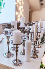 Wedding table serivce. Candles on silver vases and glasses with water stand among white flowers on wedding dinner table