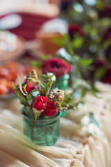 Wedding table decor. Table covered with red cloth and flowers in green vases on it