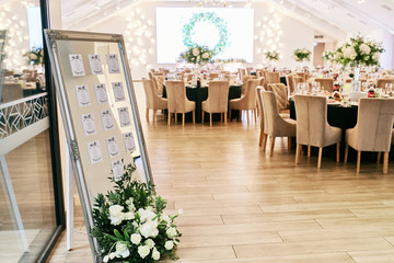 Wedding reception decor. Round dinner tables covered with pink and green clothes and served with glasses, crockery and white flowers stand in the hall