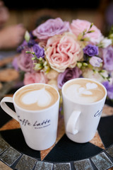 Two cups with delicious latte stand before violet wedding bouquet