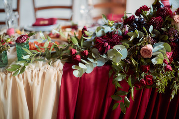 Wedding table decor. Table covered with red cloth and flowers in green vases on it