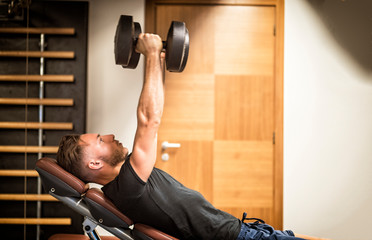 Muscular young man, training pecs on gym bench