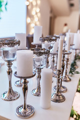 Wedding table serivce. Candles on silver vases and glasses with water stand among white flowers on wedding dinner table