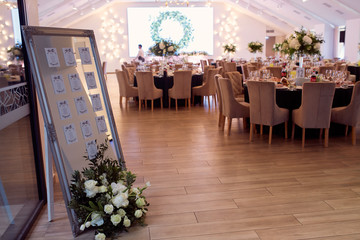 Wedding reception decor. Round dinner tables covered with pink and green clothes and served with glasses, crockery and white flowers stand in the hall