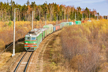 Long freight train approaches to the station at autumn day time.
