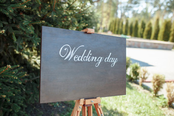 The close-up photo of the wooden plaque with the signs Welcome to the wedding standing in the street on a green banquet background. wedding decor