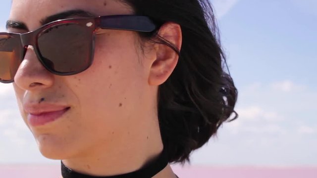 Beautiful woman is enjoying the shooting in pink lake in Mexico while touch her hair. She's wearing sunglasses on a very sunny and windy day. Cameraman is reflecting on the sunglasses