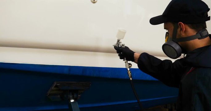 Professional master man in a robe and puller with spray gun puts a layer of paint or ceramics on the yacht. Concept of: Dangerous work, Chemistry, Paints, Garage, Transport Service.