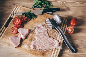 Raw white meat chicken chop and sliced tomatoes on a wooden board