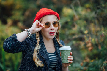 Girl in autumn park with a paper cup of hot drink