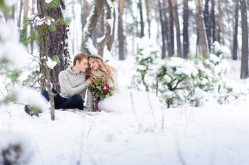 Bride and groom are sitting on the log in the winter forest. Close-up. Winter wedding ceremony.