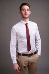 Young handsome businessman wearing eyeglasses against gray backg