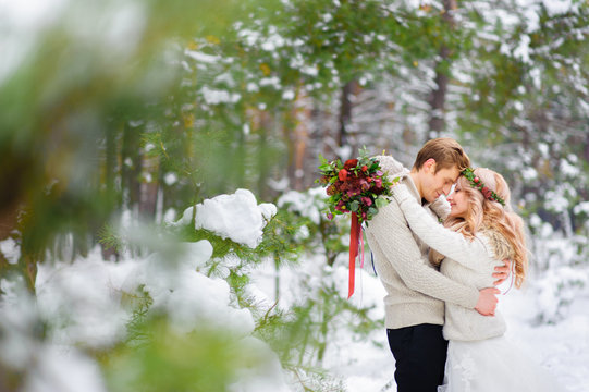 Bride and groom are sitting on the log in the winter forest. Close-up. Winter wedding ceremony.