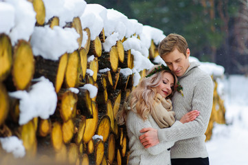 Groom kisses his bride on the temple. Newlyweds with bouquet sits on snow on the wooden background. Winter wedding