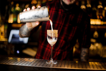 Bartender pourring a white achoholic drink from the cocktail steel shaker