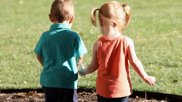 Two Kids Walking And Holding Hands As Boy Pulls His Hand Away But The Girl Grabs Him Again As They Walk Into The Grass.