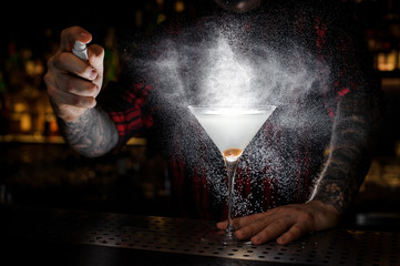 Barman spraying with essence to a Dirty Martini cocktail