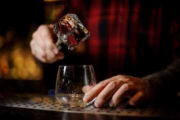 Bartender putting the ice cube to a glass preparing a James Cook cocktail