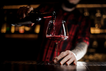 Naklejka premium Professional bartender pourring a delicious wine from a bottle to a glass
