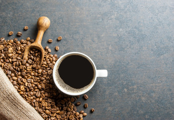 Coffee cup and beans with wooden shovel or spoon and stack of beans in burlap sack on black rustic...