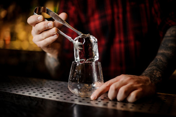 Fototapeta na wymiar Bartender hand putting a big ice cube into a whiskey dof