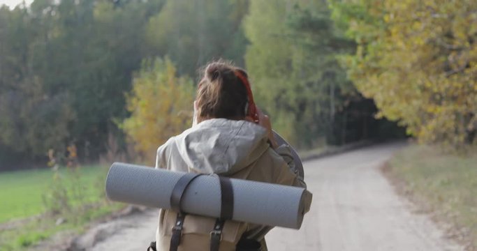 Active healthy female hipster teen model hiking along forest mountain road. Caucasian girl outdoors . Woman tourist walking in fall park on sunny autumn day. 4K video